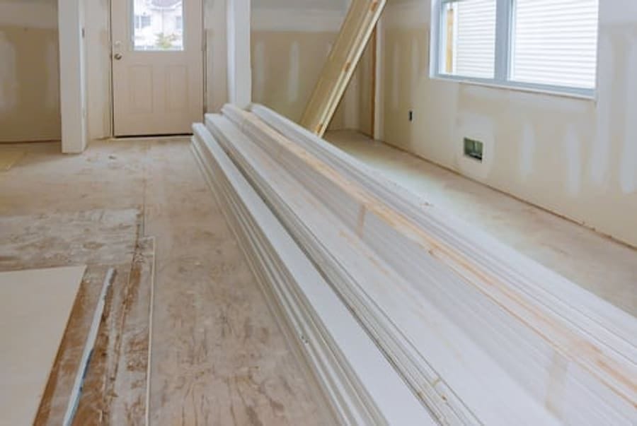 Stacked drywall sheets and trim staged inside a bright residential interior