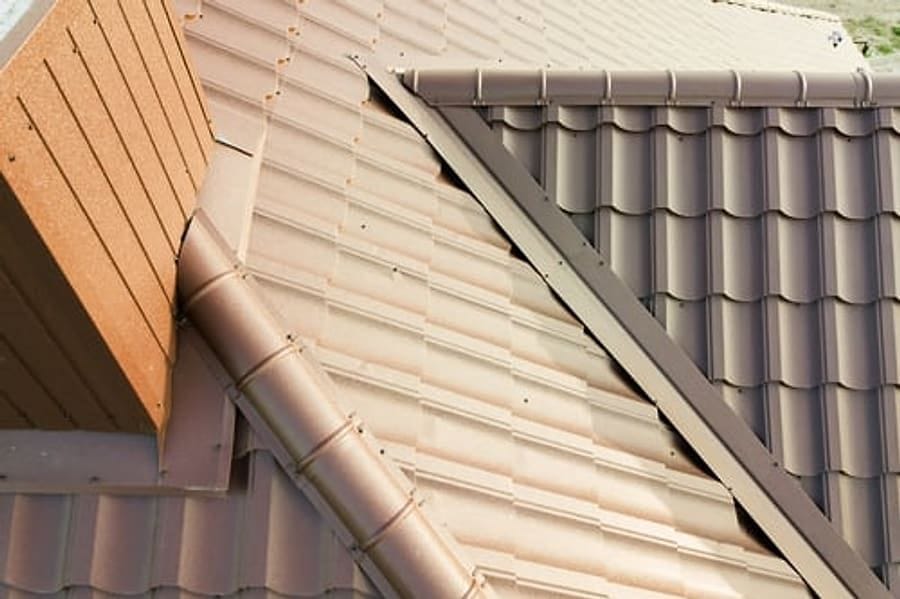 Close-up of a metal tile roof profile with matching trim and downspout