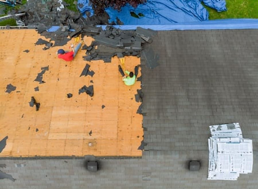 Roofing crew tearing off old shingles down to the bare deck during a replacement